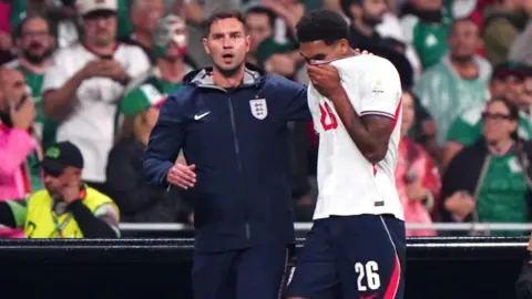 PA Media England defender Jarell Quansah walking off the pitch after he was shown a straight red card in the Three Lions win over Mexico in Mexico City. He has his head in his hands and and is being consolidated by a member of the coaching staff. 