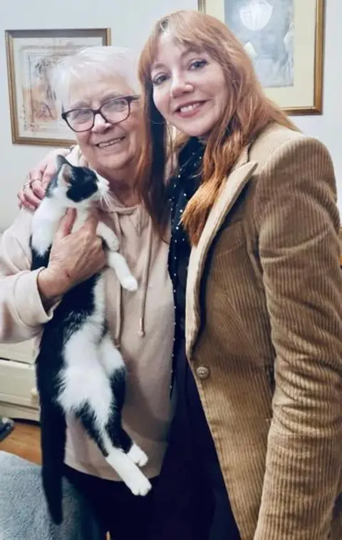 Moggies Cat Rescue Doreen Miller and Diane Morgan standing side by side. Morgan has her arm around Doreen Miller who is holding a cat