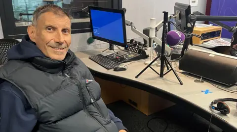 A picture of Keith Todd inside the BBC Radio Sussex studio in Brighton with Sarah Gorrell. Keith is wearing a black Berghaus gilet.