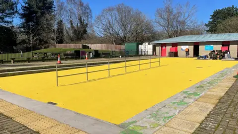 Swindon Borough Council A bright yellow, newly-laid surface at the Coate Water splash park with changing room buildings visible in the background