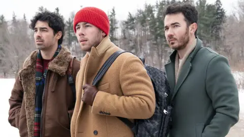 Disney/John Medland The Jonas Brothers in winter coats in a snowy landscape, standing together and looking off camera