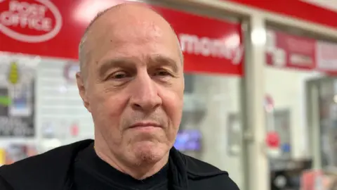 Rob is looking at the camera. He is wearing a black jacket and t-shirt. 