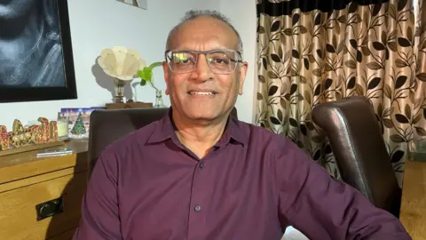 Pravin Patel wearing a maroon shirt, sitting at a table.