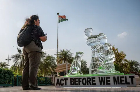 Getty Images A visitor takes a photo of the ice sculpture, melting under the heatwave in Delhi to show the impact of heatwaves across the country, as part of a protest staged by a Greenpeace activist at a mall in Delhi. The 8 foot tall sculpture shows a woman with a child and a dog - some of the most vulnerable communities affected by heatwaves and other extreme weather events