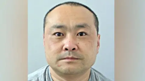 Bo Yang's mugshot. He has very dark hair in a buzzcut and brown eyes. He is wearing a grey tshirt and is against a pale grey background