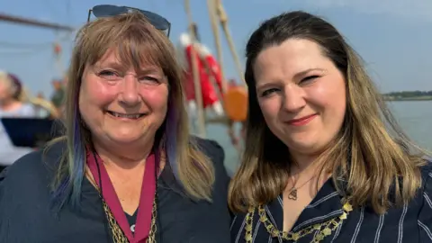 Elliot Deady/BBC Lesley Scott-Boutell wearing her mayoral chains while standing next to Jessica on a boat. She has sunglases on her head and is smiling while wearing a black top. Jessica is wearing a navy shirt with white stripes and is squinting while smiling.