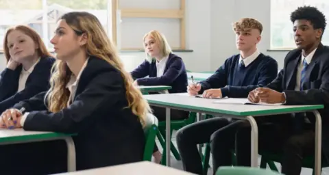 Getty Images Image shows a group of students sitting at desks in a tradition classroom setting