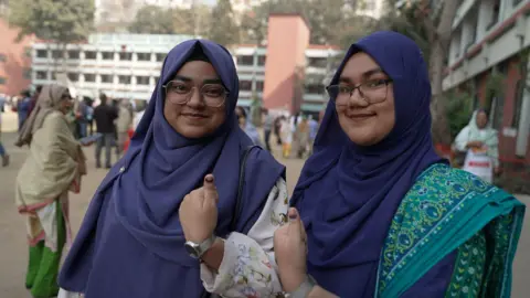 Sanjay Ganguly/BBC A couple of young women in Bangladesh smile and give the thumbs up sign
