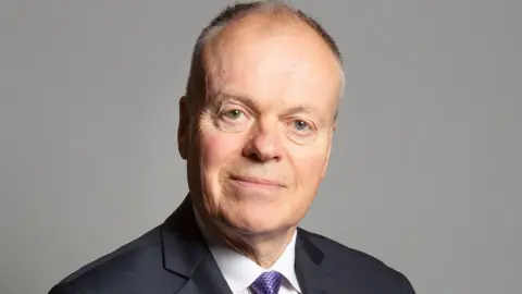 UK Parliament Official parliamentary portrait photo of Clive Betts. He has short grey hair and is wearing a black suit jacket, white shirt and purple tie.