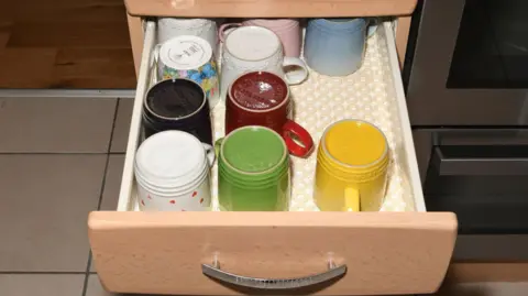 A number of mugs in an open drawer of a kitchen unit