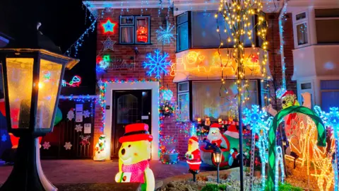 Santa's Garden The exterior of a house, covered with a large number of bright lights and other Christmas decorations.