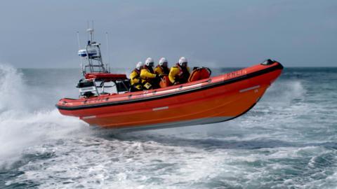 A small orange inshore lifeboat with four crew speeds through the sea.