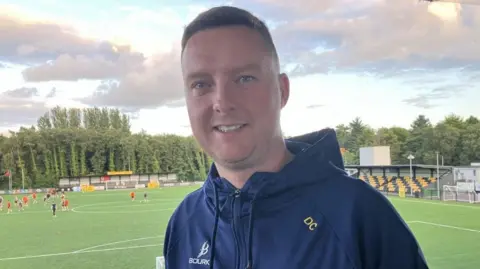 BBC Man in navy top with football pitch in background
