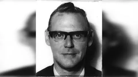 A black and white image of Anthony Littler wearing glasses and a white shirt and blazer. His hair is slicked back from his face and he is smiling slightly.