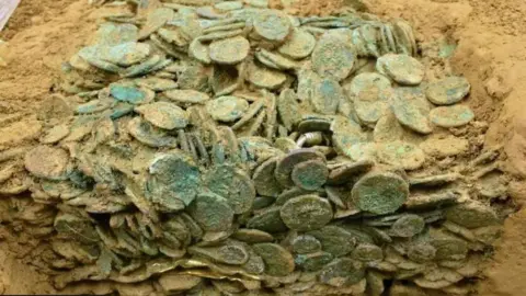 The coins when they were first discovered showing a large mass of coins together covered in dirt. 