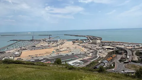 An aerial view of dover showing a road network, a large area of new tarmac and sand and land leading down to the sea with a marina