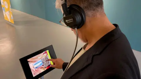A man wearing headphones touching the screen of an I-Pad.