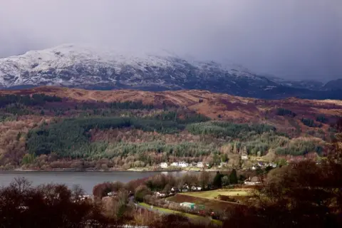 Graham Christie A snow-covered mountain range with a hill and loch below