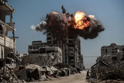 Anadolu via Getty Images A large explosion rocks a tower block, orange flame and black smoke visible. 