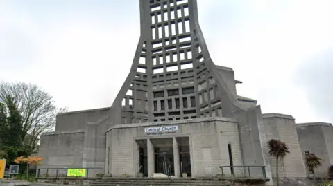 Google Google street view of Central Church in Torquay. The church is made of grey brick. There are palm trees outside the church. 