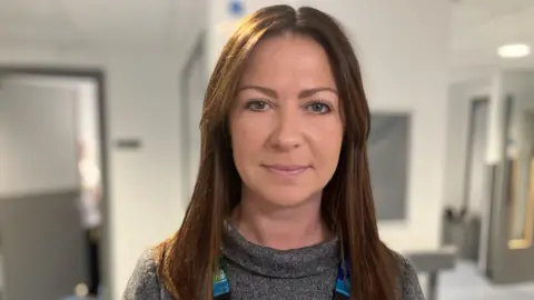 BBC Rachael Briggs wearing a grey top and multi-colour NHS lanyard.