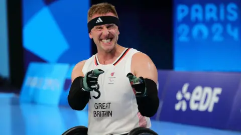 Aaron Phipps, wearing a headband and white shirt, clenching his fists and face, seemingly in celebration at the Paris 2024 Paralympic Games