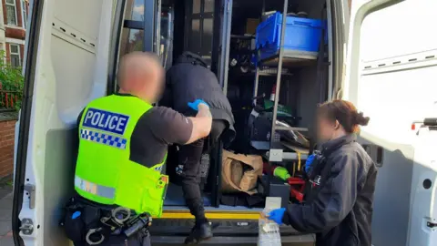 NCA Two police officers help a man into the back of a police van
