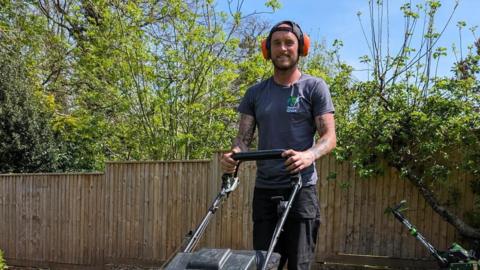 Josh Staunton stands behind a lawn mower