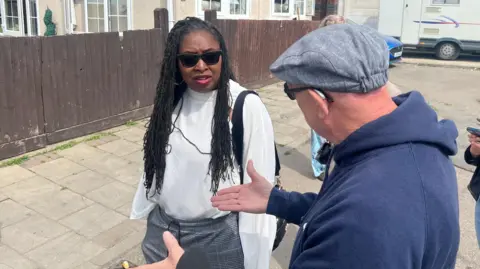 Local Labour MP, Dawn Butler speaks to Bernie Corcoran during a recent visit to the site. They are standing outside on the road. It is a sunny day.