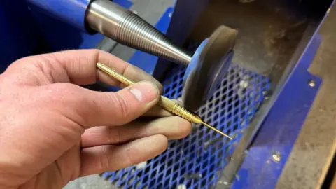 Humphrey and Hawkins One of the golden darts being sanded.