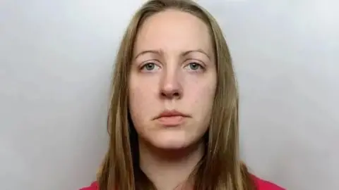 A mug shot of Lucy Letby, She is wearing a red top and wears her dark blonde hair down as she looks into the camera.