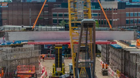 The beam is off the ground in the middle of the photo, going from left to right. A building is in the background on the right.