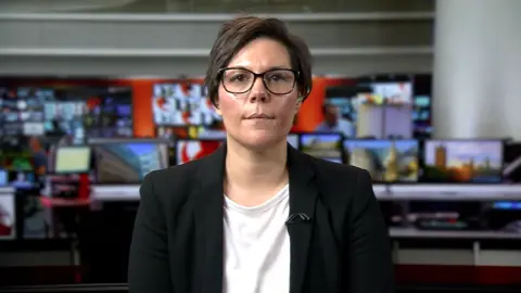 Clare Gooch, in a white T-shirt and black jacket with a television studio as a backdrop.