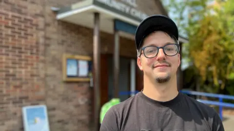 Wearing a baseball cap and dark t-shirt, David Childs-Clarke stands in front of the church community hall, where he runs a free community cafe.