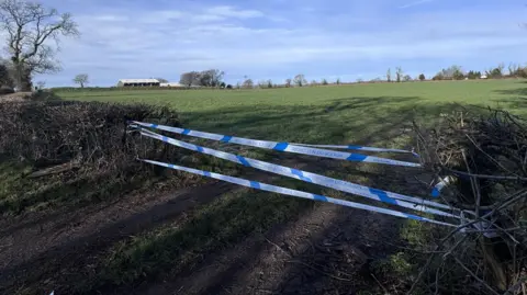 Blue and white police tape has been used to cordon off the entrance to a field.