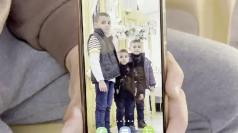 Three young Gazan boys are pictured together, facing the camera, in a photo being held up on a mobile phone.