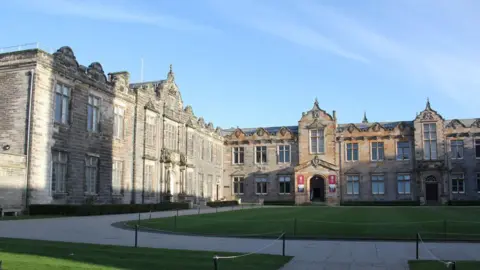 St Andrews University buildings facing onto a courtyard with a patch of grass in the middle which has a low rope around it.