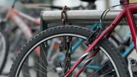 A red framed bike is secured to a bike rack with a lock.