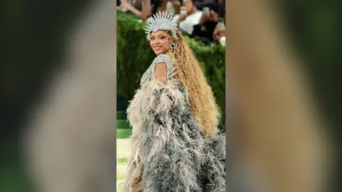 US singer Beyoncé climbing steps on Met Gala red carpet weating silver crown and feather cape