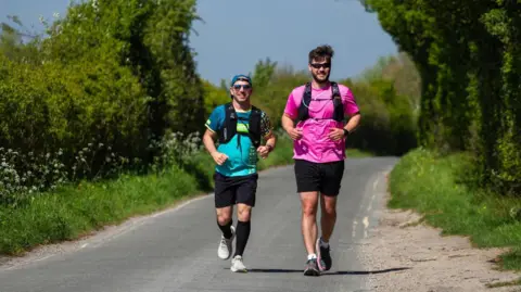 Chris running on a country road with a pacer by his side.