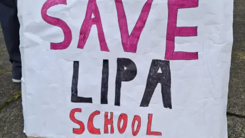 Louise King/BBC A large hand-painted banner says 'Save LIPA School'.