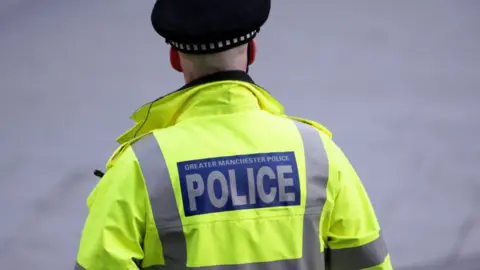 A back photo of a Greater Manchester Police officer in a green police jacket with a POLICE sign on the back