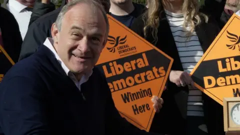 Liberal Democrat leader Sir Ed Davey with a number of supporters holding placards reading 'Liberal Democrats Winning Here".
