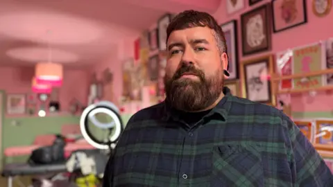 A man with brown hair wearing a blue and green tartan shirt