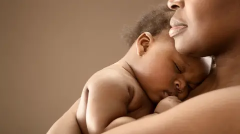 A stock image of a black mother cuddling her baby.