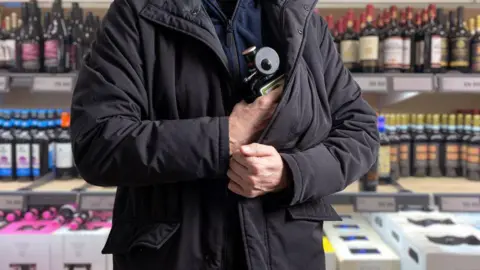 A person concealing a bottle of alcohol in the black jacket they are wearing,