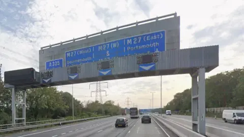 M3 gantry over motorway with blue direction signs on it and traffic seen on both sides of the motorway.