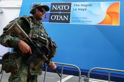 Reuters is an armed soldier in front of a blue logo of NATO