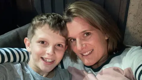 Ellen Roome A selfie of Ellen Roome and Jools Sweeney, a 14-year-old boy. They are both smiling and Ellen has her arm around Jools, her son. Jools is wearing a grey T-shirt and Ellen is wearing a pink, white and black striped long-sleeved T-shirt. They both have dark blonde hair.