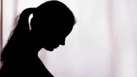 A side-on silhouette of a woman, she has her head bowed and is wearing her hair in a pony-tail.